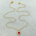 Detail van gouden hartvormige hanger met drie rode stenen en witte zirkonia-rand - Ketting