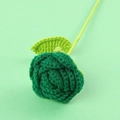 Handmade knitted rose in sage green yarn with leaf detail on matching light background - Christmas Green Rose Bouquet
