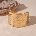 Makrodetail der goldenen Blattstruktur auf einem metallischen breiten Manschettenarmband - Gold