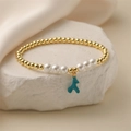 Golden beaded bracelet with pearls and a blue antler pendant on white rock - Lake Blue