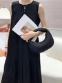 Detail of a black woven crescent handbag paired with a pleated dress and necklace - Black