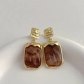 Détail de boucles d'oreilles dorées avec carrés en résine marbrée sur un socle en pierre - Marron