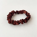 Detailopname van bruine satijnen scrunchie met glanzende textuur en plooien op leer decor - Kastanjebruin