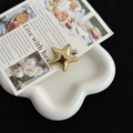 Detailed view of a metallic gold star hair clip placed on a white ceramic flower tray - Gold