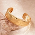Detailed relief engraving on gold oval open bangle displayed on a natural stone - Gold