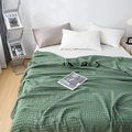 Detail of green waffle weave cotton blanket showing 3D square texture on a white bed - Green