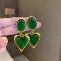 Vintage style gold oval earrings with green resin heart drop held by hand - Oval Heart Stud / Green