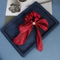 Detalle de coletero de satén rojo con lazo elegante y perla sobre terciopelo azul - Burdeos