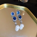 Close-up of vintage earrings with blue gemstones and white pearls on a gold mirrored tray - 56# Silver Pin Rhinestone Oval Glass Pearl Tassel Earrings