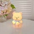 Cute bear night light with blue plaid ribbon glowing warm yellow on a white table - Small Bear Pink - Pink Ribbon