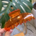 Detail of amber acrylic shark hair claw clip with golden glitter and seven teeth design - Thickened 7-Tooth Clip (Approx 10cm) / Orange Glitter