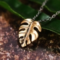 Minimalist gold Monstera leaf pendant necklace with a polished finish on green foliage - Gold