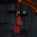 Macro shot of carved wood deity pendant with red tassel on natural branch background - Aged Cypress Nine-Tailed Fox Red Tassel