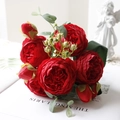 Close-up of red artificial peonies and roses with green leaves on a magazine background - Red