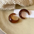 Macro shot of amber resin geometric C-shaped earrings on a ceramic dish and knit background - Brown