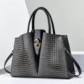 Detail of dark grey crocodile embossed leather handbag with black patent leather and gold lock - Gray