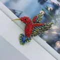 Dettaglio della spilla a colibrì con strass vivaci nei colori rosso, blu e verde smeraldo - Oro Antico + Rosso