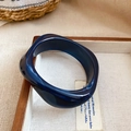 Close-up of a deep blue wavy acrylic bangle with marble texture on a vintage tray - Blue - Twisted