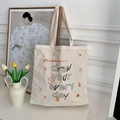 Gros plan sur le sac fourre-tout en toile beige avec typographie et imprimés artistiques - Blanc Cassé