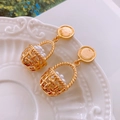 Close-up of golden basket-shaped earrings with white faux pearls on white ceramic - Gold