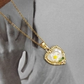 Détail d'un pendentif cœur vintage avec fleur de marguerite et perle sur chaîne dorée - Collier Pendentif Coeur Blanc