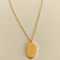 Detailed close-up of golden oval pendant with floral engraving on a fine link chain - July Larkspur