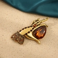 Vintage gold hand brooch with amber teardrop gem and brown crystal accents on beige background - Hand With Gemstone