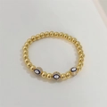 Macro shot of gold beaded evil eye bracelet with micro-pave stones on elastic band - Multicolor Evil Eye