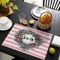 Close-up of pink striped Christmas placemat with Joy wreath on dark wood dining table - CD57-30