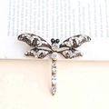 Spilla libellula dorata con cristalli iridescenti e strass su sfondo beige neutro - Bianco