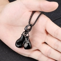 Detalle de mano sosteniendo un collar con colgante de guantes de boxeo negros - Aleación / Negro
