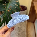 Close-up of light blue marble acetate hair claw clip held by hand showing smooth texture - Large / Water Ice Texture