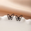 Primer plano macro de pendientes de mariposa negros calados sobre una base blanca texturizada - Negro