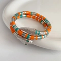 Macro detail of a coiled snake bracelet featuring green eyes and colorful enamel stripes - Bracelet / Silver/Orange/Turquoise (Green Eyes)