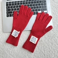 Detail of red knit wool gloves featuring lettered textile labels on a white plush background - One Size / Red