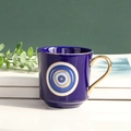 Ceramic Evil Eye coffee mug in navy blue with gold handle on elegant book stack - Sapphire Blue