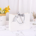 White cardboard gift bag with grey satin bow and rope handles on marble surface - 28*9*20cm / White