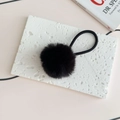 Close-up of fluffy black faux fur pom-pom hair tie on a white textured stone surface - Black