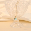 Close-up of a blue glass butterfly pendant on a gold chain inside a crystal glass - Light Blue