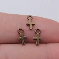 Tre ciondoli a croce in bronzo antico su un polpastrello per mostrare la misura 10x6mm - Bronzo Antico