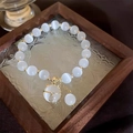 White cat eye stone beaded bracelet with golden cat bell pendant on wooden display - Lucky Cat Bracelet