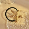 Elegant gold starfish charm hair tie with elastic black band on a textured glass plate - Golden Starfish