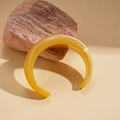 Artistic close-up of amber resin open bangle cuff on textured stone element - Yellow