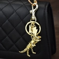 Golden dinosaur skeleton keychain with lightning charm attached to a black leather handbag - Gold