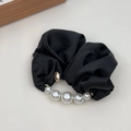 Close-up of black satin hair scrunchie with elegant imitation pearls and gold hardware - Black