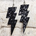 Dettaglio di orecchini neri a forma di fulmine glitterati con paillettes su fondo in pietra - Nero Argento Glitter