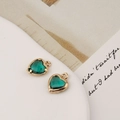 Détail de deux pendentifs cœur en cristal vert avec monture dorée posés sur un livre - 10*12mm / Vert