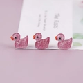 Close-up of three pink glitter resin duck miniatures in a row on a lavender backdrop - Fuschia