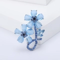 Elegante spilla a fiore argento con cristalli blu e strass su un piedistallo bianco - Blu