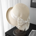 Beige woven straw bucket hat with a large bow and gold metal logo on a wooden stand - Off-White (80468# Letter D)